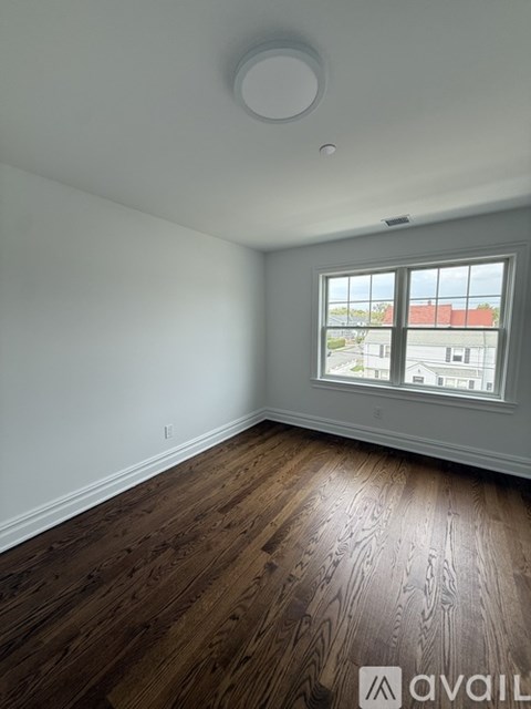 A room with wooden flooring and a window overlooking a building.
