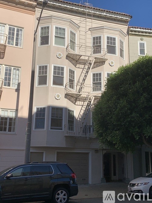 A grey SUV is parked in front of a building with a tree to the right.