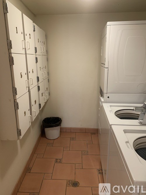 A laundry room with a washer and dryer and a trash can.