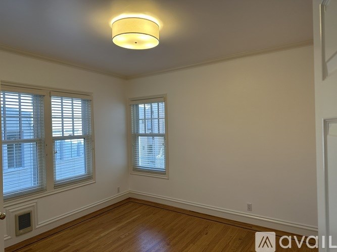 A room with wooden floors and two windows with blinds.