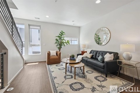 A living room with a black couch, a wooden table, and a rug with a geometric pattern.