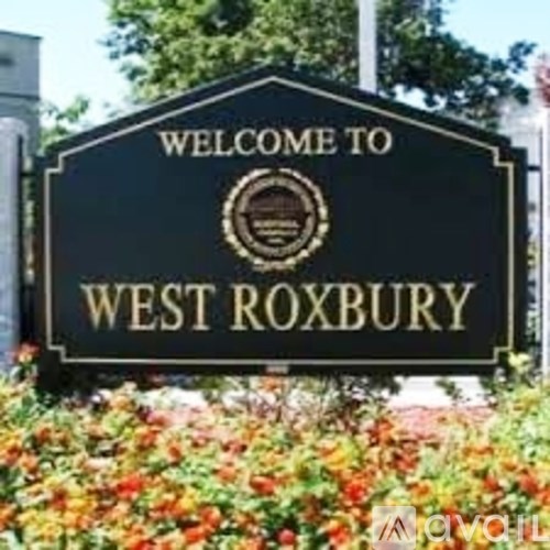 A sign that says "Welcome to West Roxbury" is displayed in front of some flowers.