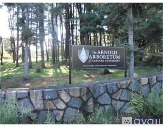 A sign for The Arnold Arboretum of Harvard University is displayed in front of a stone wall.