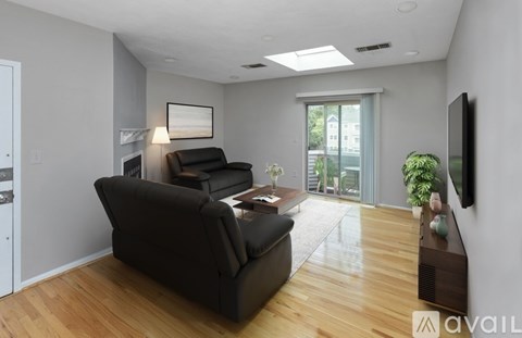 A living room with a black leather couch and a flat screen TV mounted on the wall.