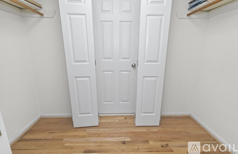 A white door is in the middle of a room with wooden floors.