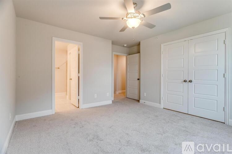 A room with a carpeted floor, a ceiling fan, and three doors.