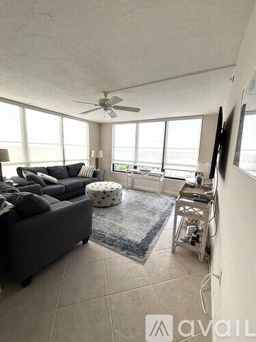 A living room with a grey couch, a blue rug, and a ceiling fan.