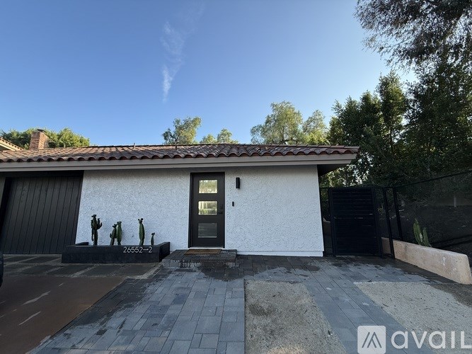 A white house with a black door and windows, and a statue of three people in front.
