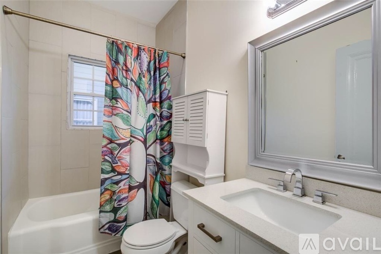 A bathroom with a white toilet, a white sink, and a shower curtain with a tree pattern.