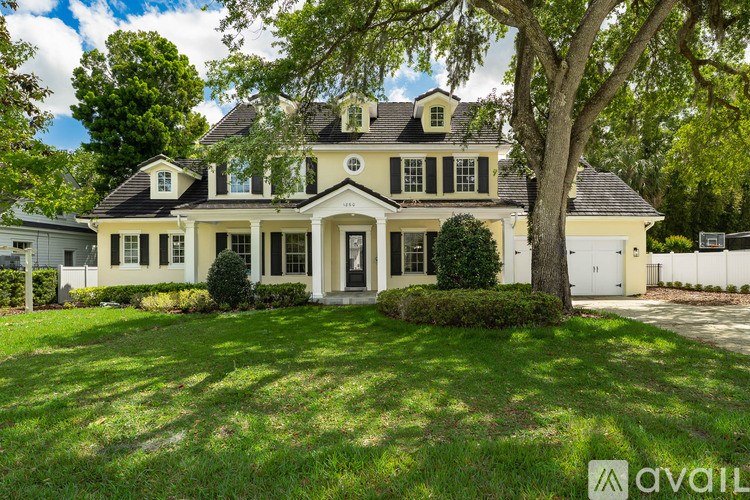 A large, two-story house with a white front door and a large tree in front.