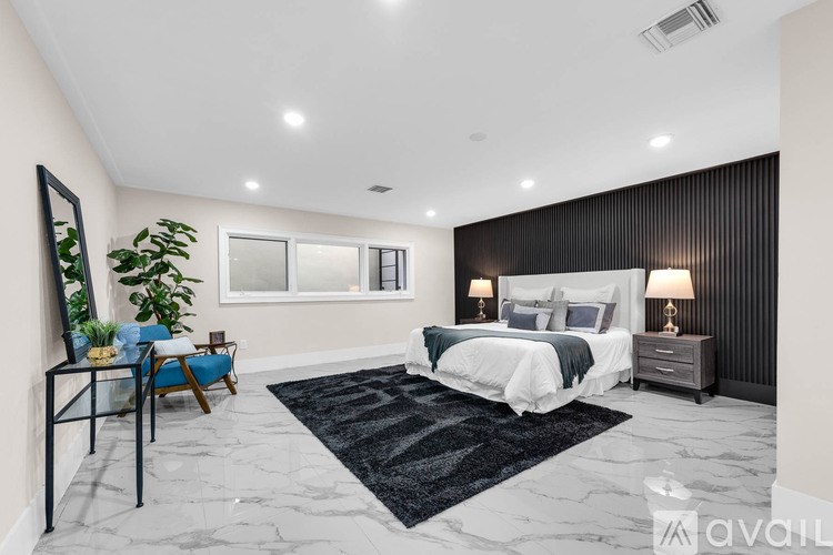 A bedroom with a large bed, a chair, and a potted plant.