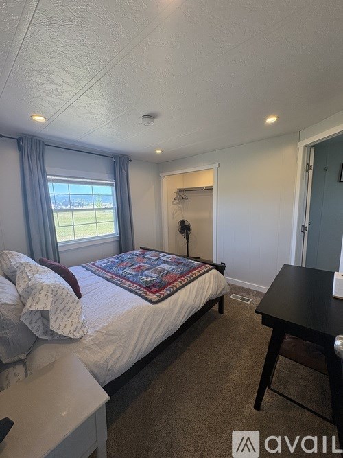 A bedroom with a bed, a small table, and a window with curtains.