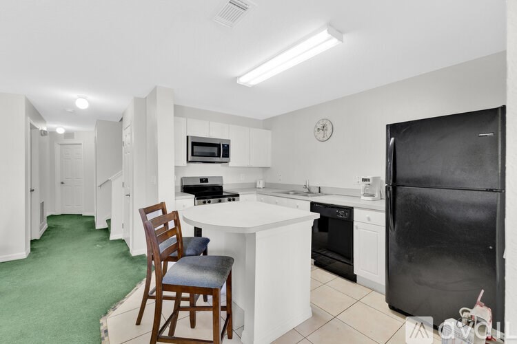 A kitchen with a black fridge, white cabinets, and a green rug.