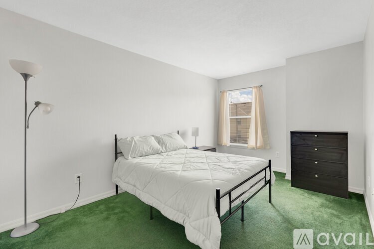 A bedroom with a white bed and green carpet.
