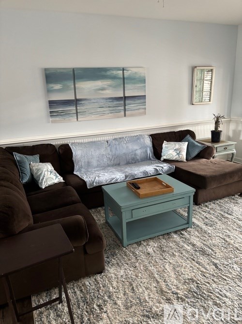 A living room with a brown couch, a blue cushion, a green coffee table, and a painting on the wall.