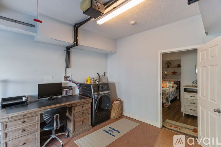 A room with a desk, chair, and a washing machine.