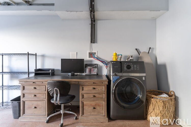 A room with a washing machine and a desk with a computer.