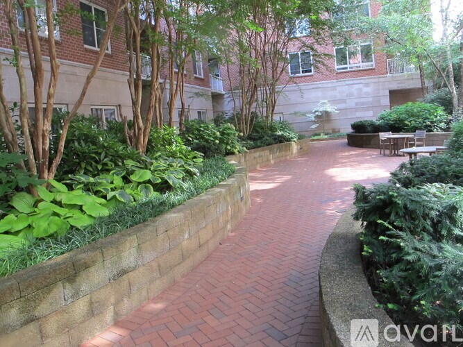 A brick pathway leads through a landscaped area with trees and shrubs.