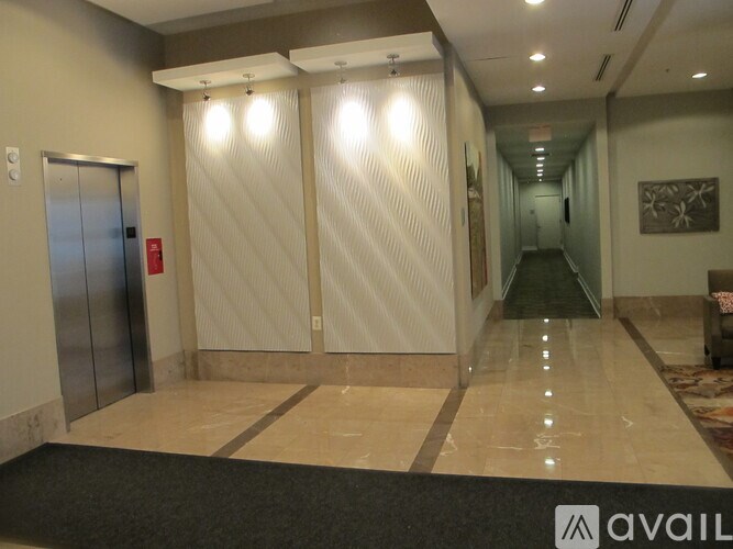 A hallway with a carpeted entrance, a wall-mounted artwork, and a closed elevator.