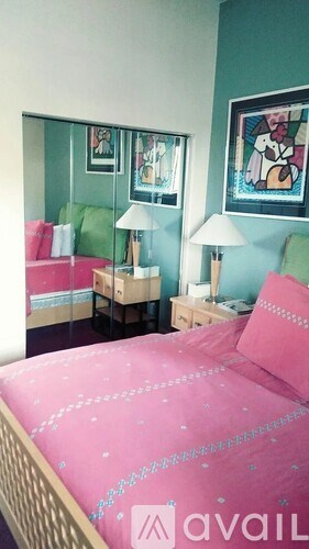 A bedroom with a pink bedspread and two nightstands with lamps.