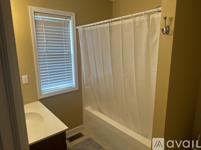 A bathroom with a white shower curtain and a window with blinds.