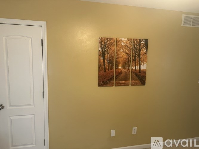 A painting of a tree-lined road is hanging on a wall.