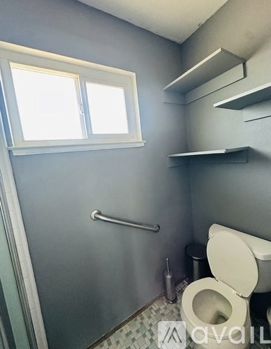 A bathroom with a toilet, a window, and a grab bar.