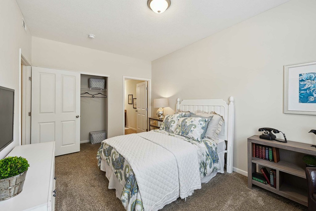 A bedroom with a bed, nightstand, and a plant.