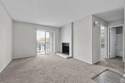 A sparsely furnished living room with a fireplace and sliding glass doors.