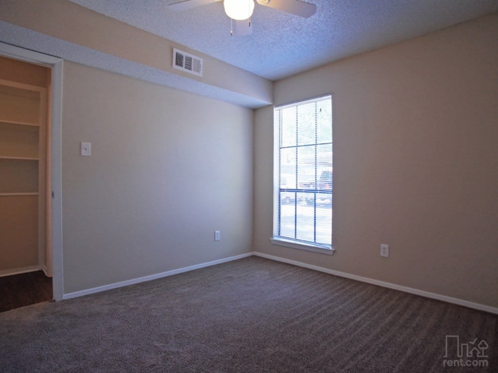A room with a carpeted floor, a window, and a ceiling fan.