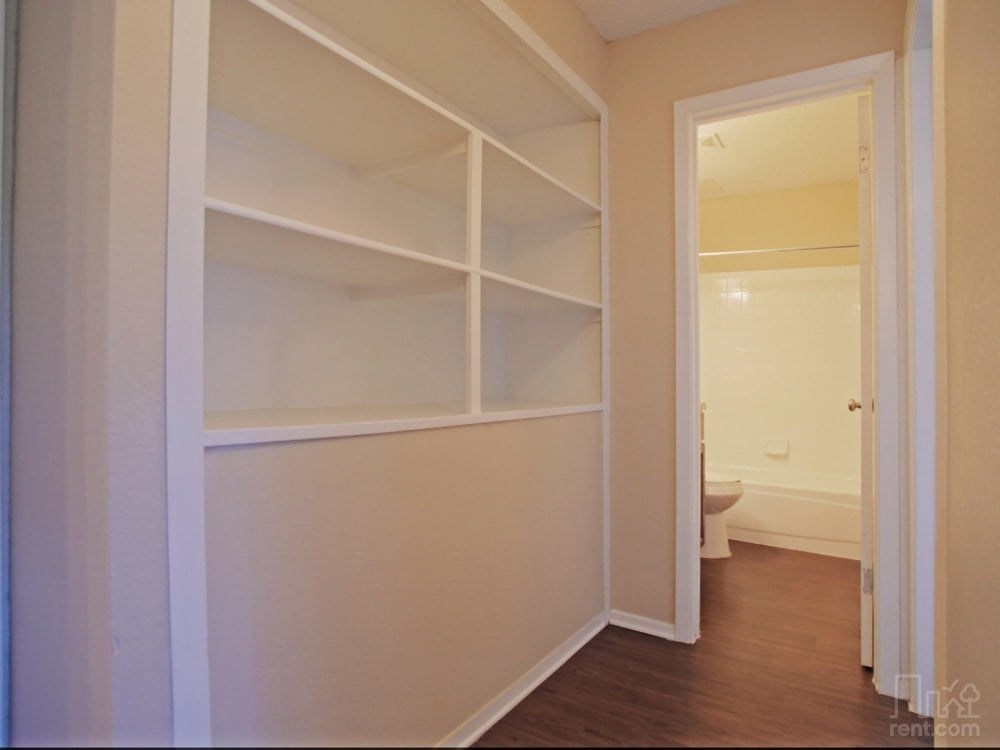 A white closet with shelves and an open door leading to a bathroom.