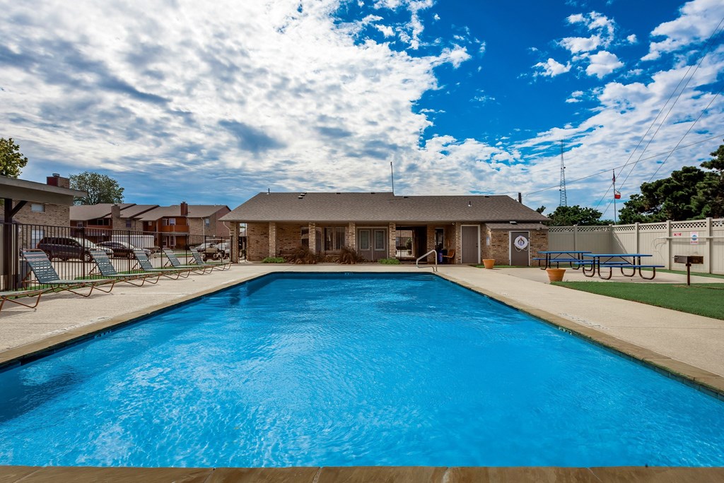 A large swimming pool in front of a building with a blue sky and clouds in the background.