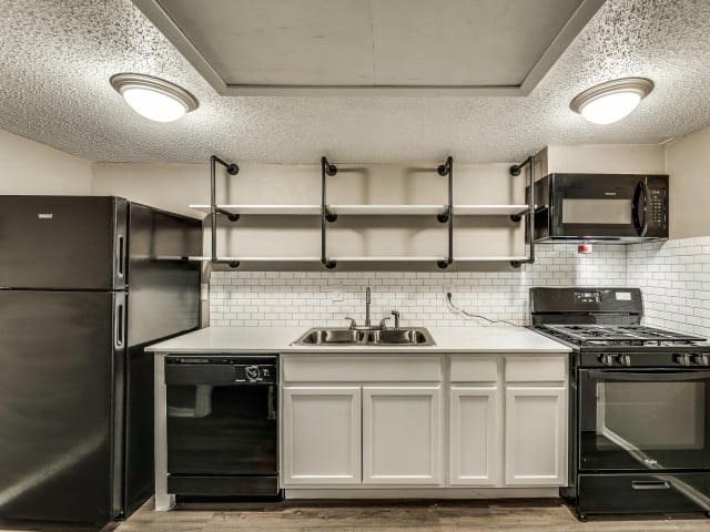 A kitchen with a black refrigerator, white cabinets, and a black stove top oven.