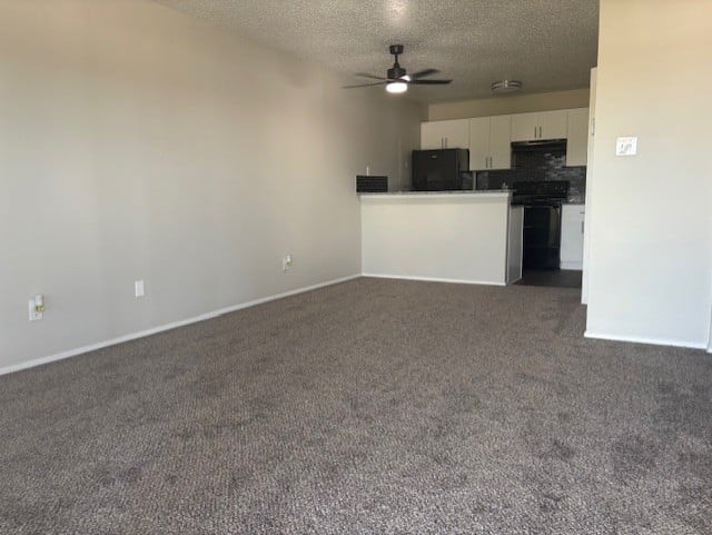 A room with a ceiling fan and a kitchenette in the corner.