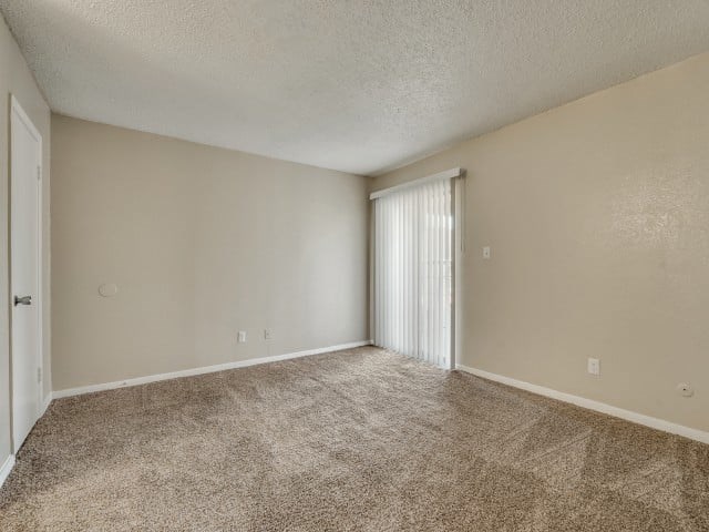A room with a carpeted floor and a window with blinds.