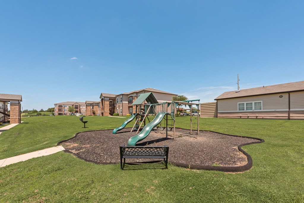A playground with a green slide and a bench in the foreground.