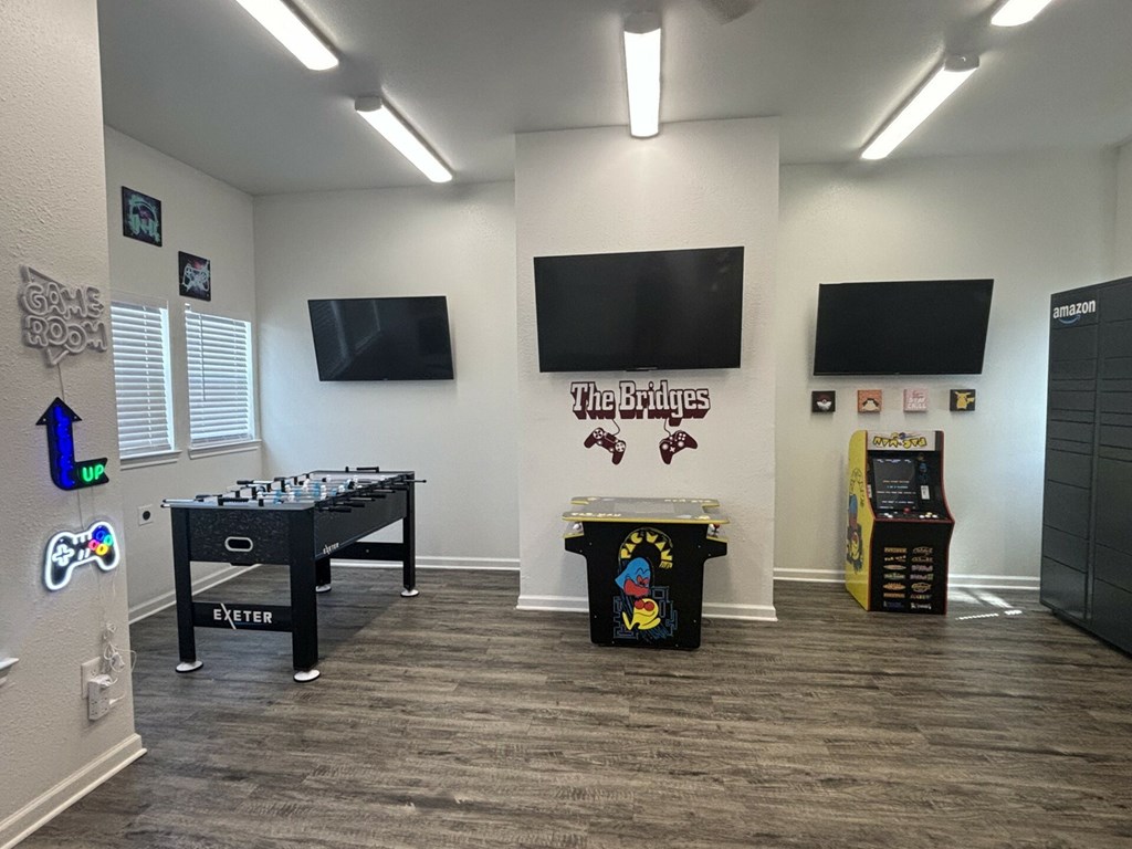 A room with a foosball table, a trash can with a basketball design, and a wall with a banner that reads "The Bridges."