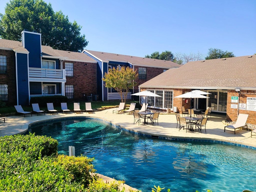 A swimming pool surrounded by chairs and umbrellas in front of a building.