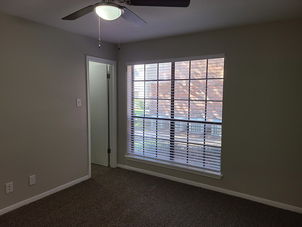 A room with a ceiling fan and a window with blinds.