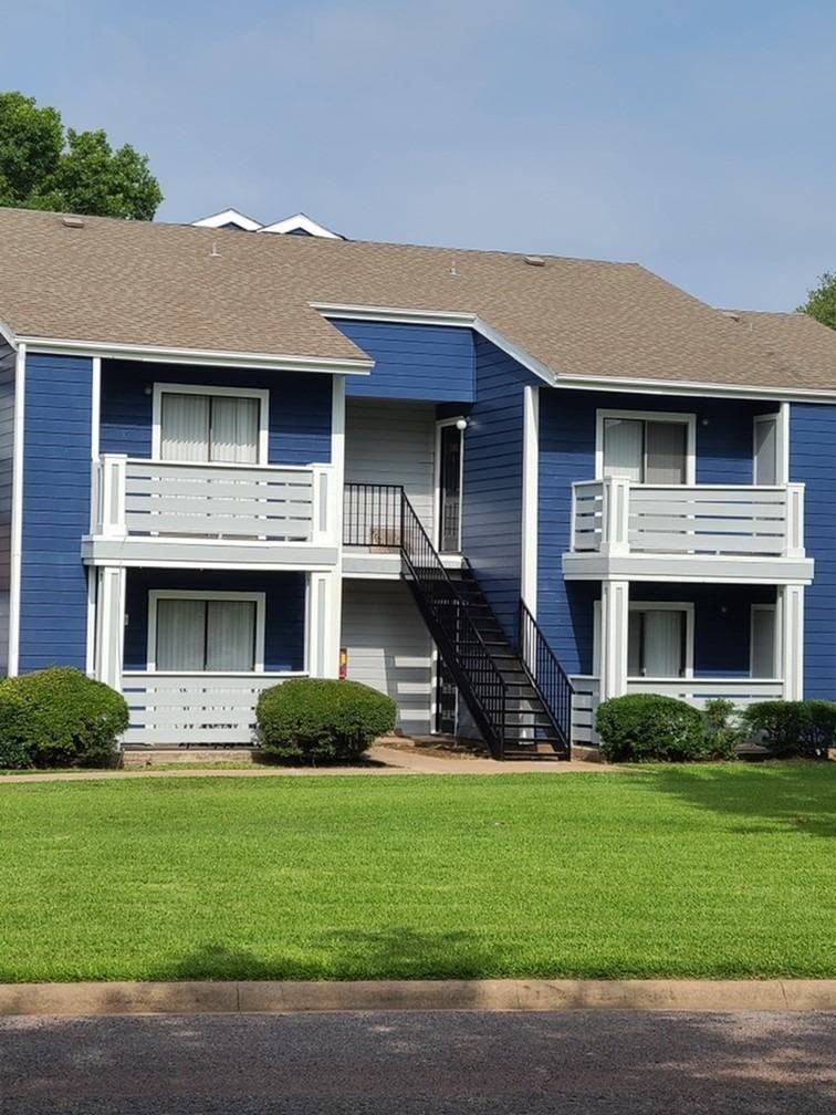 A blue and white two story apartment building with a green lawn in front.