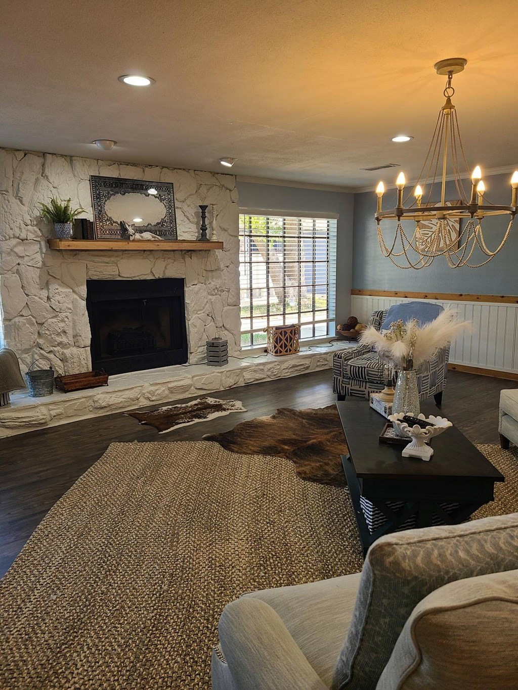 A living room with a stone fireplace and a chandelier.