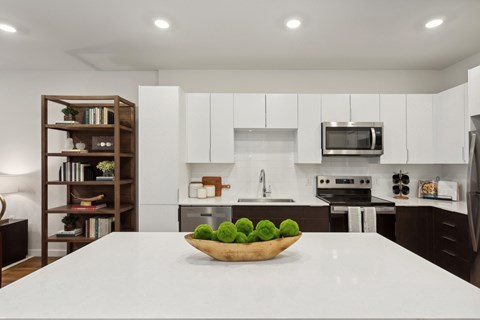 A bowl of green apples sits on a white countertop in a modern kitchen.