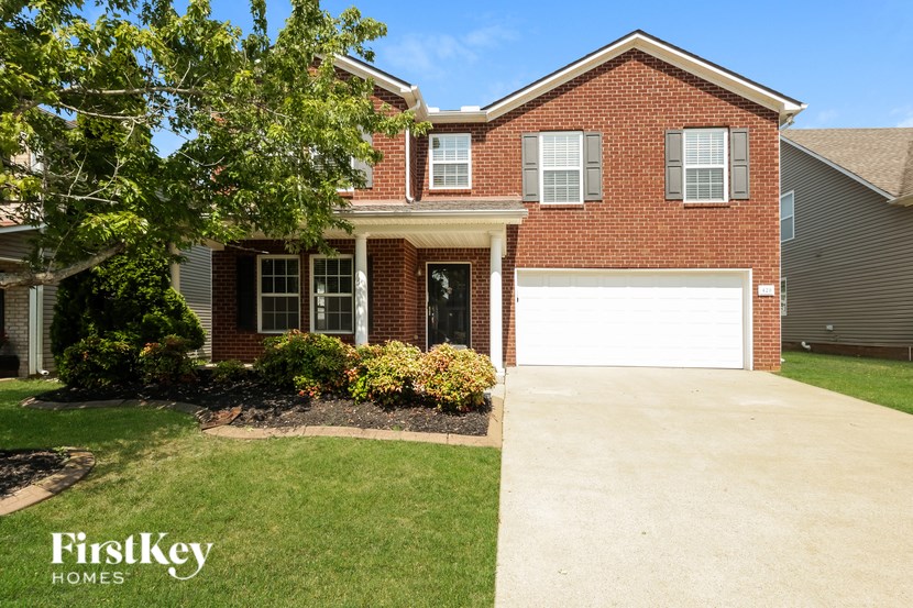 A brick house with a garage door and a tree in front.