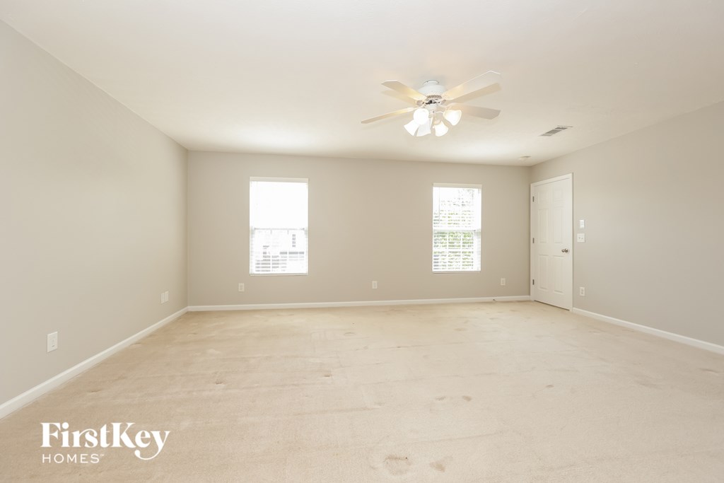 A spacious room with a ceiling fan and two windows.