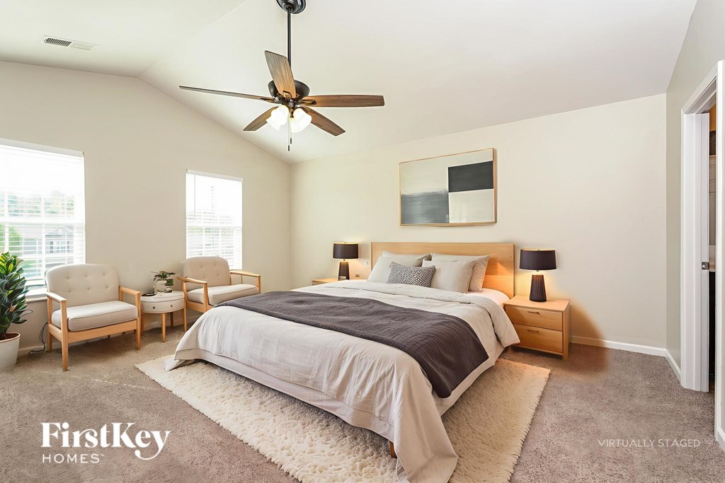 A bedroom with a bed, two chairs, and a ceiling fan.