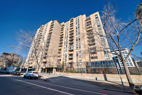 A tall building with a lot of windows is surrounded by trees and cars on the street.