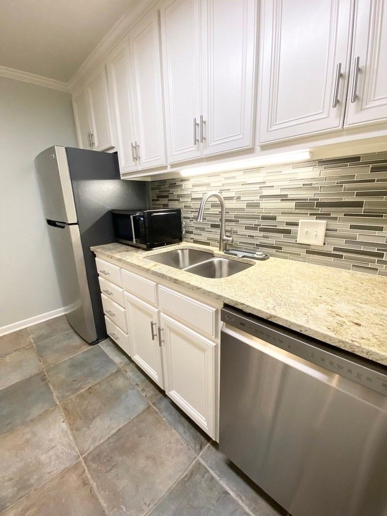 A kitchen with a black fridge, white cabinets, a microwave, and a granite countertop.