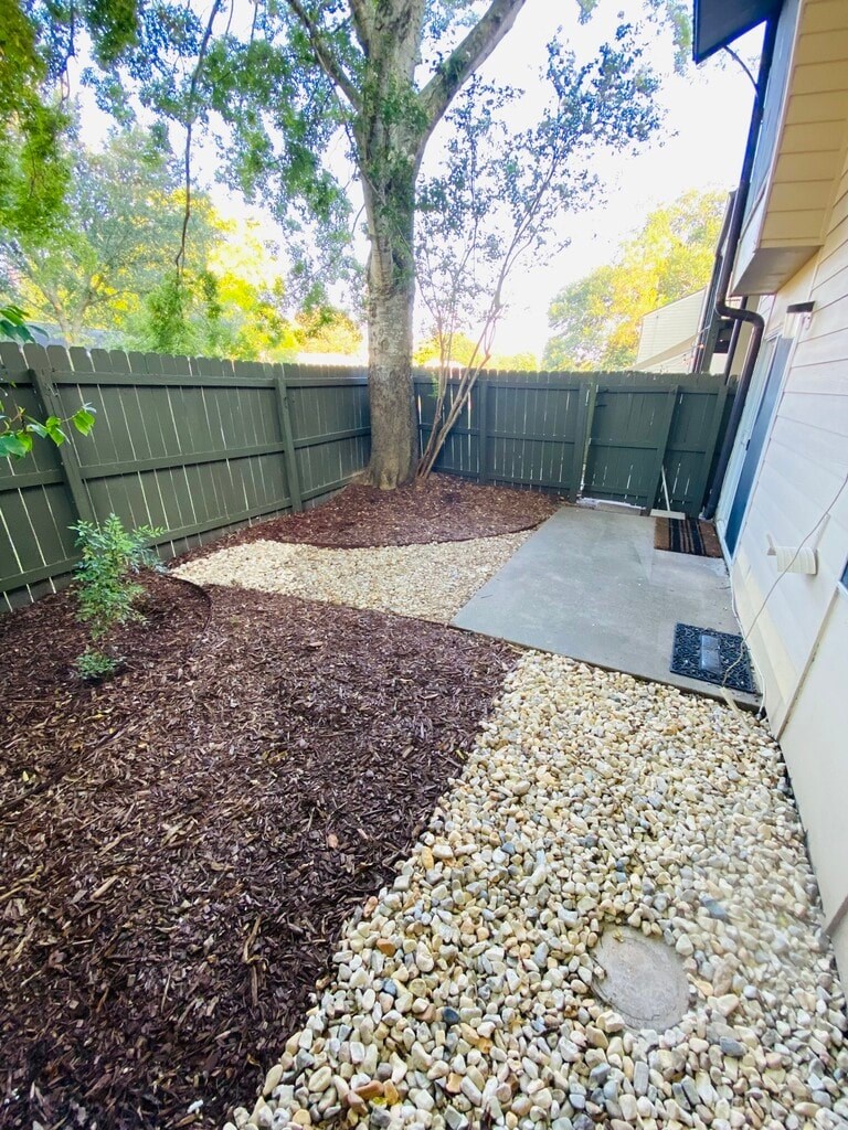 A backyard with a brown mulched area, a gravel area, and a green fence.