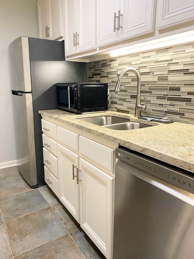 A kitchen with a black fridge, white cabinets, and a tiled backsplash.