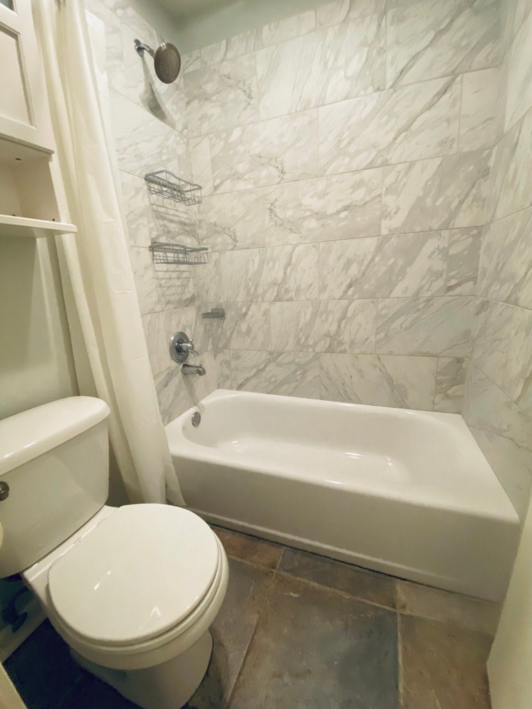 A white toilet sits next to a white bathtub in a bathroom with marble tile walls.